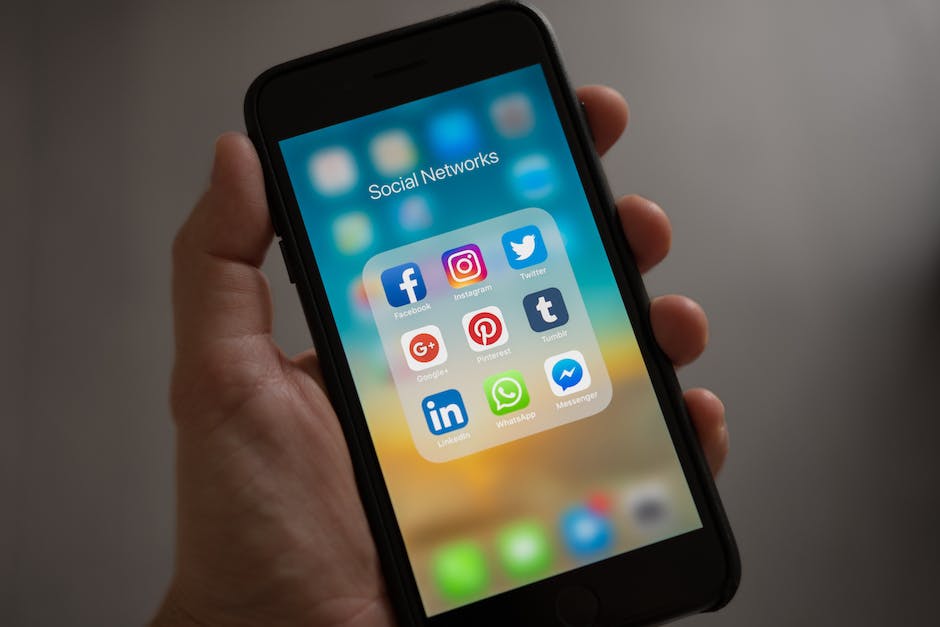 This is an image of a person holding a smartphone with different social media apps on the screen. There are icons for Facebook, Instagram, Twitter, and LinkedIn, among others. The image shows how social media can be used by businesses to connect with their audience and promote their brand.